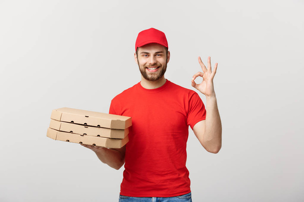 Conceito de entrega: Bonito homem de entrega de pizza fazendo sinal OK isolado sobre fundo cinza
. - Foto, Imagem