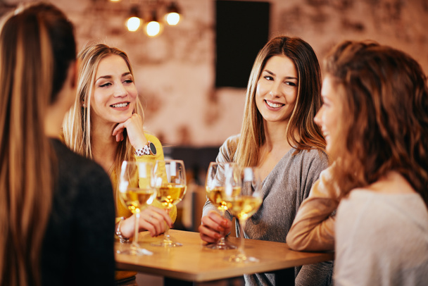 Female friends drinking wine and chatting while sitting in the bar. - Photo, Image