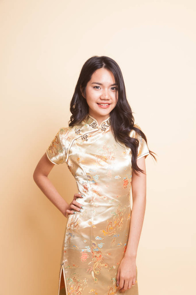 Portrait of Asian girl in golden chinese cheongsam dress on beige background - Valokuva, kuva