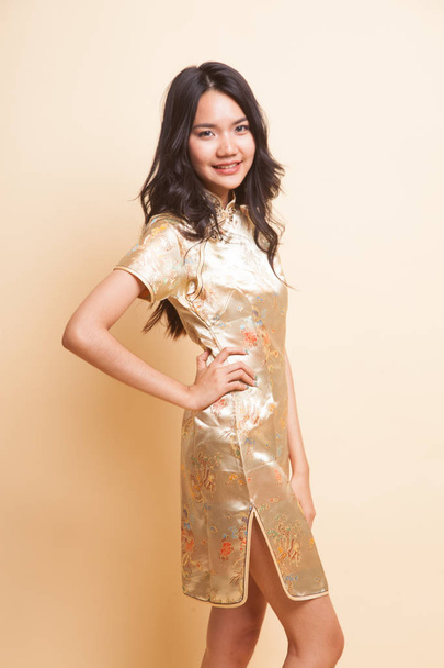 Porträt eines asiatischen Mädchens im goldenen chinesischen Cheongsam-Kleid auf beigem Hintergrund - Foto, Bild