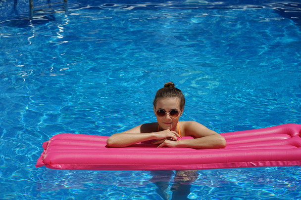 Nainen seisoo uima-altaassa pitäen ilmapatjaa
 - Valokuva, kuva