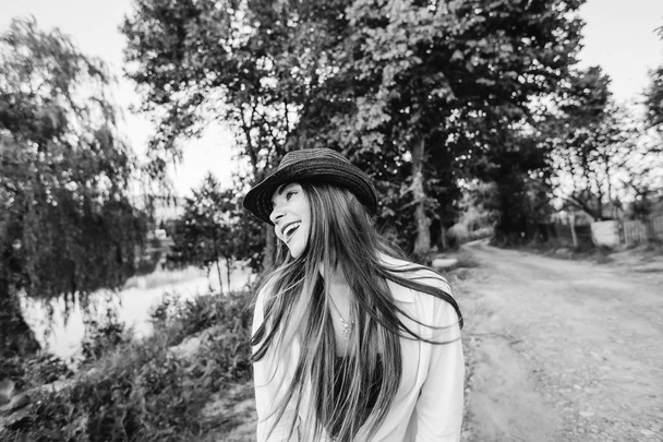 meisje met een hoed op haar hoofd kijken naar de zijkant tegen de achtergrond van de natuur op een zwart-wit foto - Foto, afbeelding