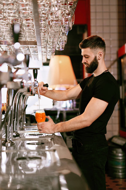 Bartender Working At Bar Pub. Handsome Man Pouring Draught Beer In Glass. High Resolution. - Foto, imagen
