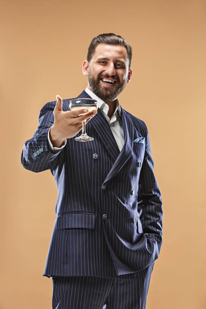 Smiling young businesman with glass of champagne standing and celebrating over pastel background - Foto, Imagen