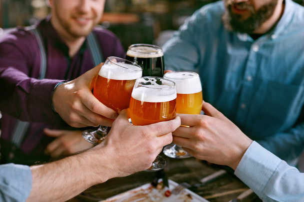 Drinking Beer. Friends Raising Glasses Of Beer At Table With Food In Pub Bar. High Resolution. - Photo, Image