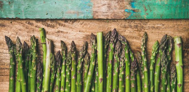 Raw uncooked green asparagus in row over rustic wooden background - Foto, Bild