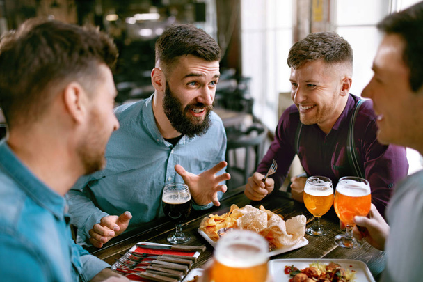 Friends At Dinner Drinking Beer And Eating Food In Pub Restaurant. High Resolution. - Fotografie, Obrázek