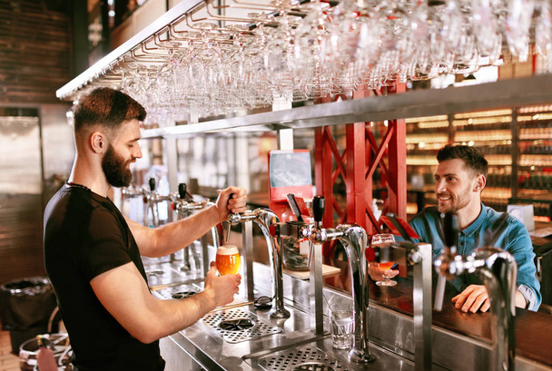 Beer Pub. Bartender And Customer In Bar. Man Pouring Beer From Tap In Glass At Bar Counter. High Resolution. - Photo, image