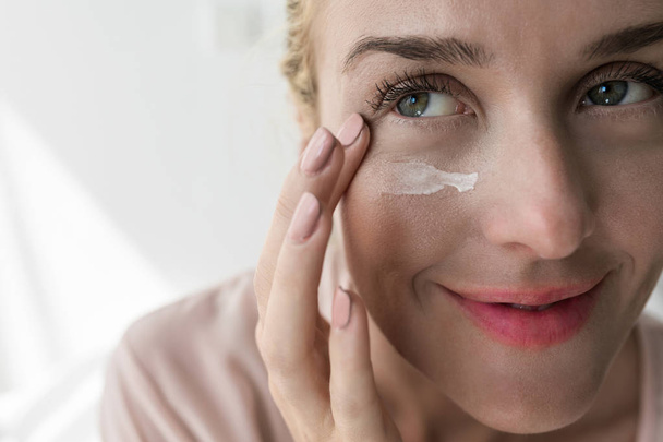 Pretty Caucasian woman applying skin care creme under eye. - Fotó, kép
