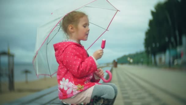 Esernyő játék az eső jégkrém evés a parton gyönyörű kislány - Felvétel, videó