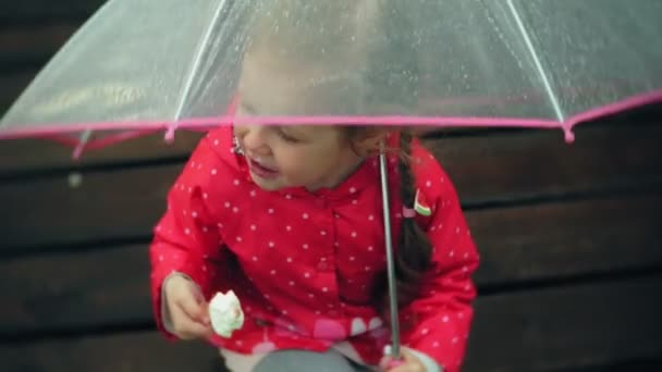 Little beautiful girl with umbrella playing in the rain eating ice cream on the coast - Footage, Video