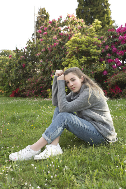 16-jähriger Teenager sitzt in einem Park mit Gras und Blumen, aufgenommen in Limousinen, Frankreich. - Foto, Bild