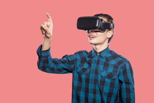 young man wearing checkered shirt with vr headset touching imaginary screen on pink background   - Foto, Imagen