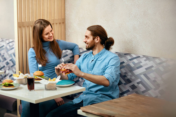 Couple With Burgers. Man And Woman Eating Fast Food In Cafe. High Resolution. - Valokuva, kuva