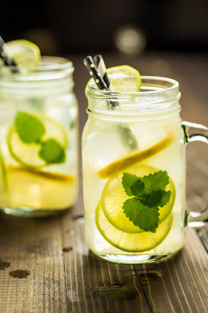 Коктейль Cold Fresh Lemonade Mojito Cocktail with Ice, Lemon and Mint Leaves в Mason Jar на деревенском фоне. Лето
. - Фото, изображение