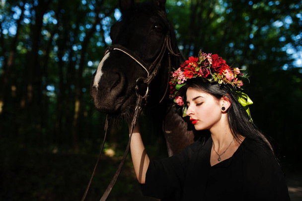 Mystical girl in wreath wear in black with horse in wood. - Foto, afbeelding