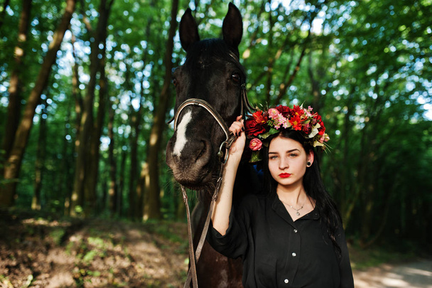 Mystical girl in wreath wear in black with horse in wood. - Foto, Imagen