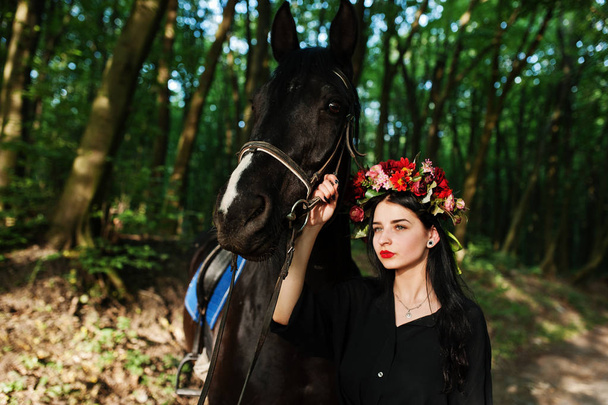 Mystical girl in wreath wear in black with horse in wood. - Fotoğraf, Görsel