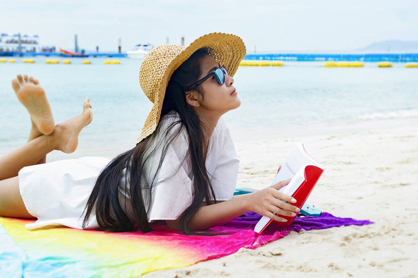 Mulher feliz sorrindo e ler livros na praia em um belo. Menina bonita asiática em casual olhando para longe e sorrir, rindo. A praia bela no céu brilhante
 - Foto, Imagem