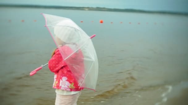 Trochę piękna dziewczyna z parasolem, grając w deszczu, spacery wzdłuż wybrzeża - Materiał filmowy, wideo