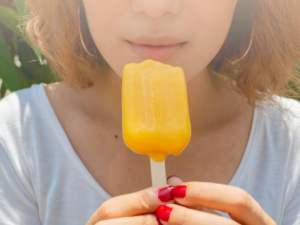 Piękne kobiety na sobie białą koszulę jeść żółty Popsicle lodu Pop topnienia na czas letni w promieniach słońca na tle drzewa krótkie włosy - Zdjęcie, obraz