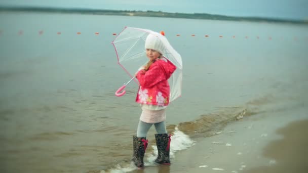 Krásná holčička s deštníkem, hraní v dešti, procházek podél pobřeží - Záběry, video