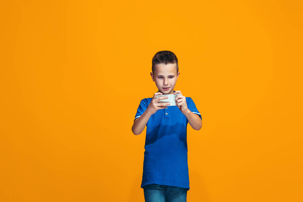 The happy teen boy standing and smiling against orange background. - Фото, изображение