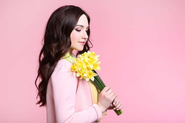 Beautiful woman in fashion clothes with narcissus flowers on pink background - Fotó, kép