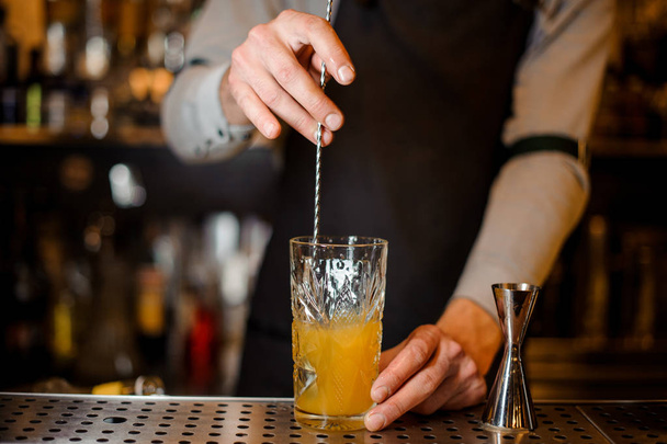 Cantinero revolviendo una bebida de naranja alcohólica en el hermoso vaso en el mostrador de barras de acero
 - Foto, Imagen