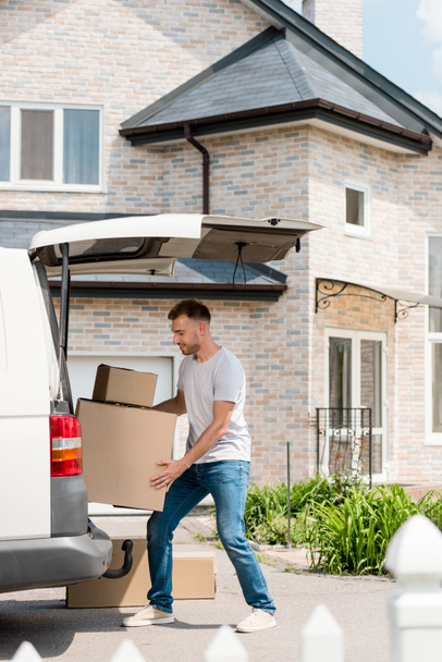  Молодой улыбчивый мужчина передвигает коробки из машины в новый дом
  - Фото, изображение