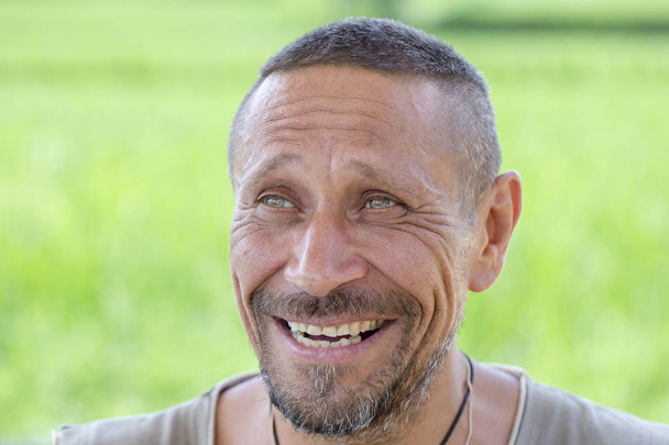 People and lifestyle concept. Happy middle-aged unshaven man with cheerful smile outdoor against green nature background. Adult man portrait close up - Zdjęcie, obraz