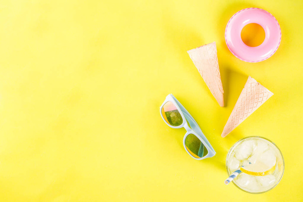Summer holidays vacation concept background, hat, sunglasses, cooling drink (lemonade, mojito) with ice, ice cream cones, Lifebuoy yellow background copy space flatlay above - Foto, Imagem