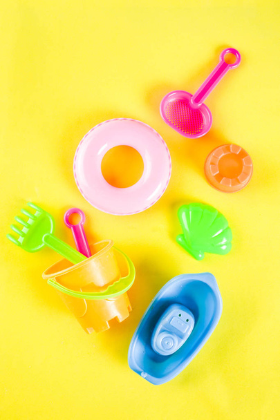 Summer vacation concept with plastic beach kids toys - bucket, scoop, rake, molds boat, lifebuoy toys copy space yellow background - 写真・画像