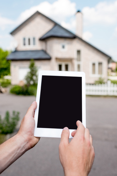 częściowy widok mężczyzny trzymającego cyfrowego tabletu z pustego ekranu przed domek  - Zdjęcie, obraz