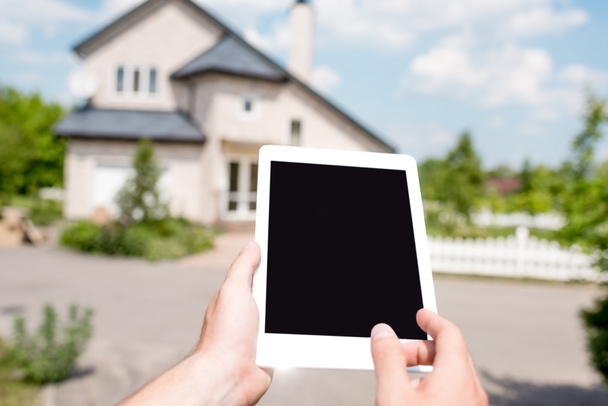 cropped image of man holding digital tablet with blank screen in front of cottage  - Photo, image