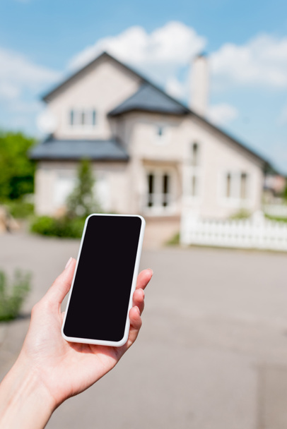 recortado de mujer joven sosteniendo teléfono inteligente con pantalla en blanco en frente de la casa
  - Foto, imagen