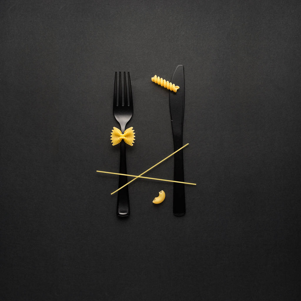 Creative still life photo of fork and spoon with raw pasta on black background. - Fotoğraf, Görsel