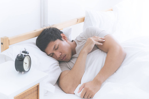 Азиатский мужчина спит на белой кровати с будильником
 - Фото, изображение