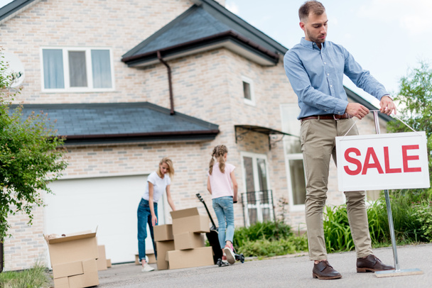 чоловічий ріелтор вішає знак продажу перед людьми, що переїжджають з дому
 - Фото, зображення