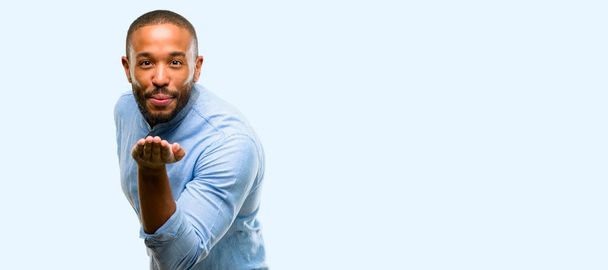 African american man with beard expressing love, blows kiss at camera, flirting isolated over blue background - Photo, Image