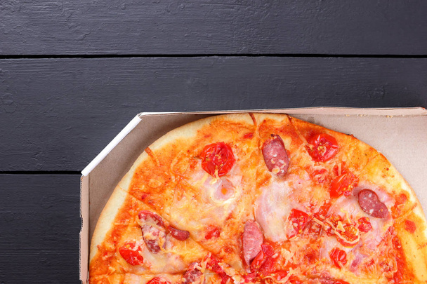 Pizza on a black wooden background, Italian pizza with tomatoes, bacon, sausages and cheese, fast food, festive food on a dark background, copy space, American cuisine - Φωτογραφία, εικόνα