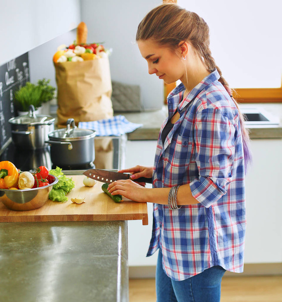Молода жінка ріже овочі на кухні біля столу
 - Фото, зображення