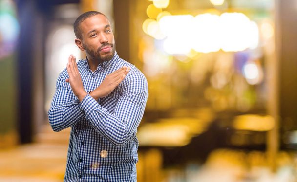 Uomo afroamericano con la barba infastidito dal cattivo atteggiamento che fa segno di stop incrociando le mani, dicendo di no, esprimendo sicurezza, difesa o restrizione di notte
 - Foto, immagini