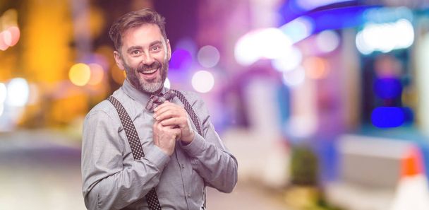 Mann mittleren Alters, mit Bart und Fliege selbstbewusst und glücklich mit einem großen natürlichen Lächeln im Nachtclub - Foto, Bild