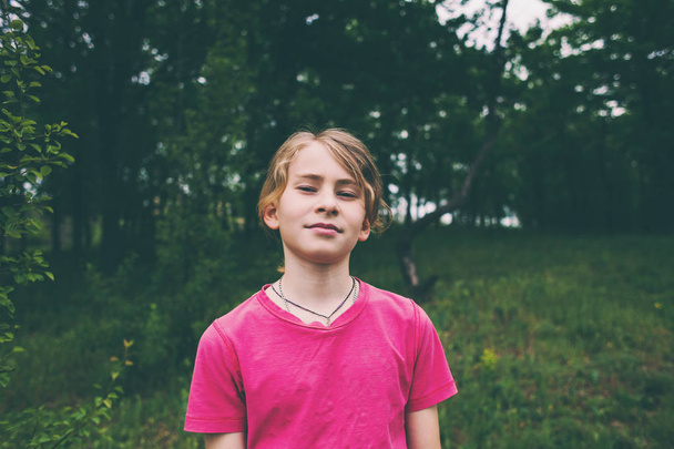 Portrait of a boy in the forest. Portrait of a child. Blond in the background of trees. A teenager with long hair. - Photo, Image