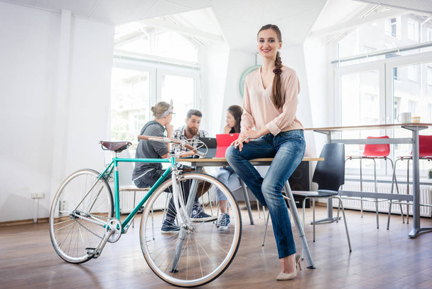 Fiduciosa giovane donna seduta su una scrivania vicino alla sua bicicletta pendolare
 - Foto, immagini
