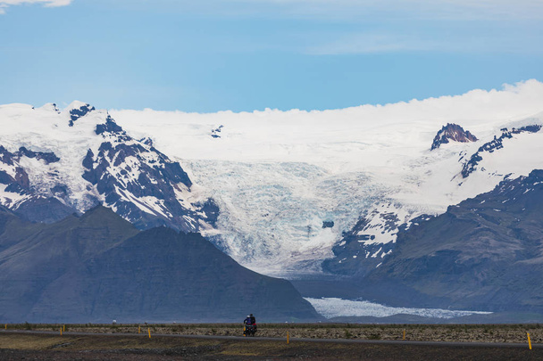 two lonely bike riders on the main road, large glacier tongue of the Vatnajoekull in background on Iceland - Photo, Image