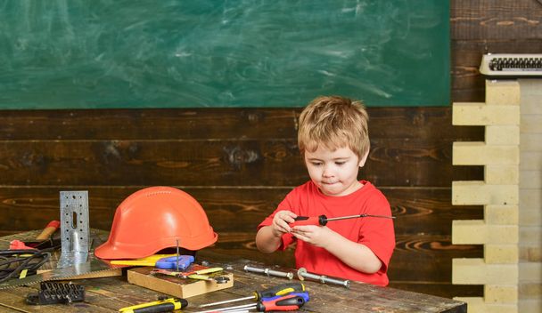 Kid playing with red screwdriver. Small boy in workshop. Tools lying on wooden table - Foto, Imagem