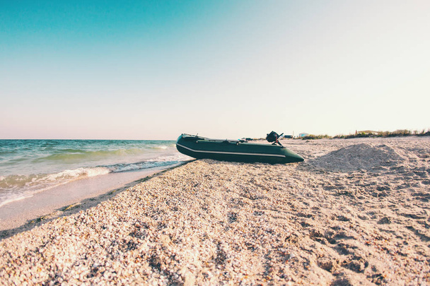 Barco inflable en la playa. Costa del mar. Hermosa puesta de sol junto al océano. Barco a motor en la orilla
. - Foto, imagen