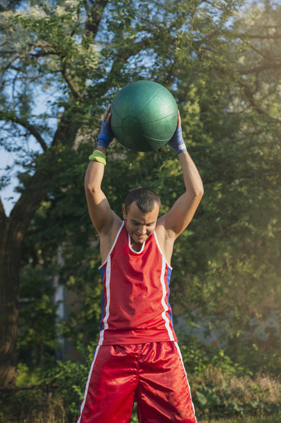 Young athlete performs sports exercises with a ball outdoors - Fotoğraf, Görsel